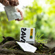 Hand Holding a Single-Serve Coffee Sachet Over a Box in a Forest Setting