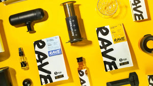 Assorted coffee-making gear, Rave Coffee packaging, and small bottles arranged on a bright yellow background, featuring an AeroPress and various coffee accessories.