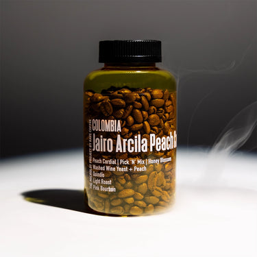 A bottle of coffee beans with a black cap, filled with roasted coffee beans, standing on a white surface against a dark gray background with dramatic lighting and a hint of smoke.