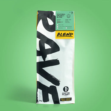 A 1 kg white and black bag of Seasonal Organic Coffee Blend Nº 7 from RAVE stands upright on a green background, ideal for organic coffee subscriptions and supporting 1% for the Planet.