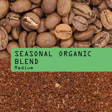 Close-up of whole Guatemalan coffee beans next to ground coffee, separated by a green label reading Seasonal Organic Coffee Blend Nº 7 in bold black text.