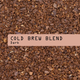 A close-up of dark brown coffee grounds with a beige label that reads 