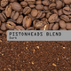 Coffee beans on top and brewed coffee granules below, with a gray label across the center reading 'PISTONHEADS BLEND Dark'.