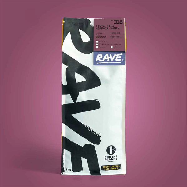 A white 1kg RAVE COFFEE bag of Costa Rica Hermosa Honey Nº 318 stands upright on a purple background, featuring “1% for the Planet” and “Great Coffee, Made Simple” text. Honey processed coffee details visible on the label.