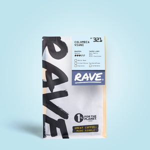 A white and yellow RAVE COFFEE bag labeled Colombia Viani Nº 321 stands on a light blue background, featuring washed Colombian coffee with black cherry and milk chocolate notes. The 1% For The Planet logo is also shown.