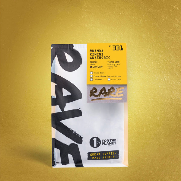 A white and yellow RAVE COFFEE bag labeled Rwanda Kinini Anaerobic Nº 331 stands on a gold background, featuring the Kinini Washing Station, fruit-forward notes, roast details, and the 1% for the Planet logo.