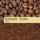 Close-up of whole Burundi Izuba Nº 334 coffee beans above ground coffee, separated by a beige label reading BURUNDI IZUBA Nº 334 Dark in black typewriter font—showcasing RAVE COFFEE’s sweet cup profile.
