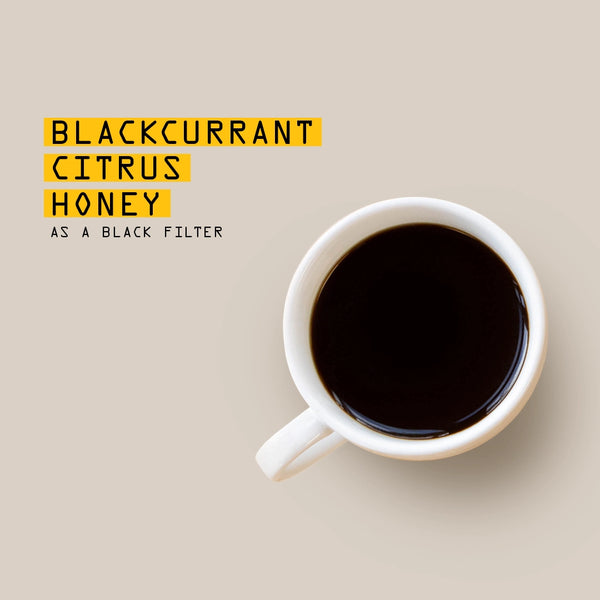 A white ceramic cup filled with black coffee on a light beige background, next to yellow text that reads 'BLACKCURRANT CITRUS HONEY AS A BLACK FILTER'.