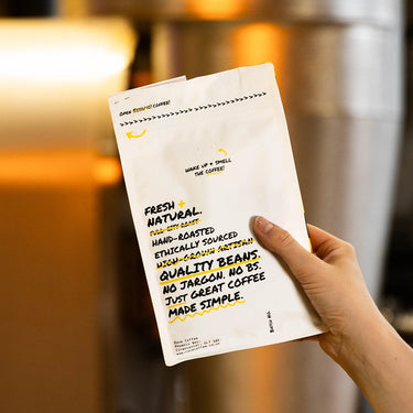 Hand holding a coffee package with text about quality and ethical sourcing.