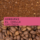 Coffee grounds and coffee beans with 'Honduras El Chollo' label on a pink background