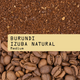 Coffee grounds and coffee beans with 'Burundi Izuba Natural' label on a beige background