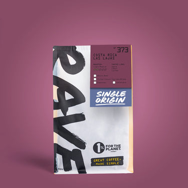 A package of One Coffee single-origin Costa Rica Las Lajas coffee, standing upright against a solid mauve background. The bag is white with bold black brushstrokes, a dark purple label, and a blue 'Single Origin' badge.