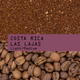 Ground coffee beans labeled 'COSTA RICA LAS LAJAS Light/Medium' with a top layer of dark roasted coffee granules and a bottom layer of whole coffee beans.
