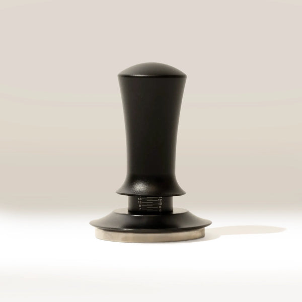 The RAVE Coffee Self Levelling Spring Tamper features an ergonomic black handle, metallic base, and measurement markings for precision tamping in 54mm espresso filter baskets. It stands upright on a light surface with a neutral background.