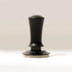 The RAVE Coffee Self Levelling Spring Tamper features an ergonomic black handle, metallic base, and measurement markings for precision tamping in 54mm espresso filter baskets. It stands upright on a light surface with a neutral background.