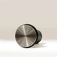 A matte black cylindrical Self Levelling Spring Tamper by RAVE Coffee, featuring a metallic concentric circular pattern on its front, is shown lying on its side against a plain light background, sized for a 54mm espresso filter basket.