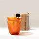 An 8oz Huskee Renew translucent orange coffee cup with a ridged texture from Huskee sits in front of a brown HuskeeRenew box on a light surface against a neutral background.