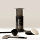 The Aeropress AeroPress Coffee Maker by Aeropress comes with a scoop, stirrer, filter holder, and round paper filters—neatly arranged on a light surface with a neutral background—ideal for brewing coffee at home.