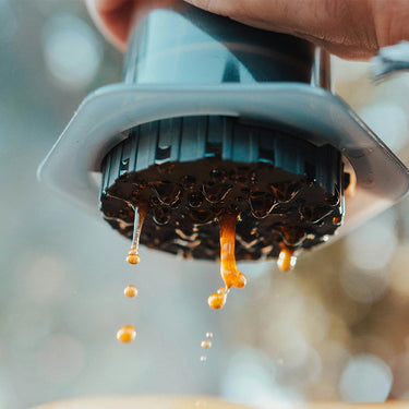 A hand presses the AeroPress Coffee Maker by Aeropress, with fresh coffee dripping below—ideal for home coffee brewing enthusiasts.