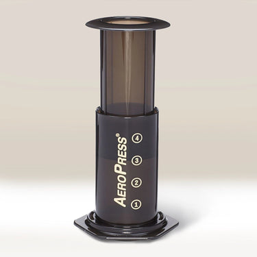 The AeroPress Coffee Maker by Aeropress, in black with numbers 1–4 and branded on the side, stands upright on a light surface against a neutral background—ideal for home coffee brewing.