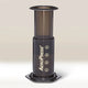 The AeroPress Coffee Maker by Aeropress, in black with numbers 1–4 and branded on the side, stands upright on a light surface against a neutral background—ideal for home coffee brewing.