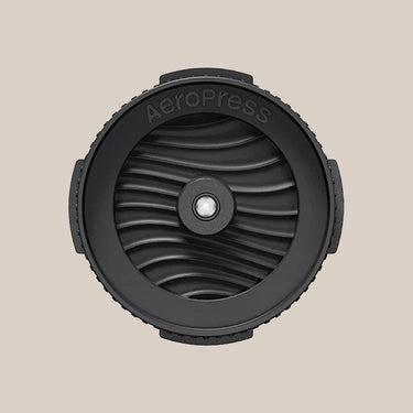 Top view of the AeroPress Flow Control Filter Cap by Aeropress, in black with a wave-like pattern and 