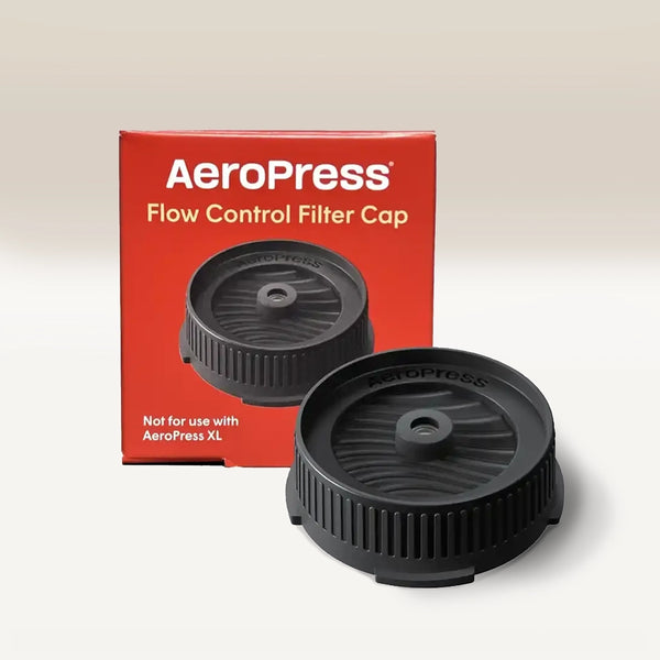 The black AeroPress Flow Control Filter Cap by Aeropress is displayed before its red box, which features white text and the cap image. The box notes it’s not for AeroPress XL. The pressure-actuated valve enables espresso-like crema.