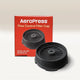 The black AeroPress Flow Control Filter Cap by Aeropress is displayed before its red box, which features white text and the cap image. The box notes it’s not for AeroPress XL. The pressure-actuated valve enables espresso-like crema.