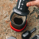 A hand presses an Aeropress Go Gift Set coffee maker by Aeropress over a cup of freshly brewed coffee set on a rough stone surface, with a black coffee scoop and lid nearby.
