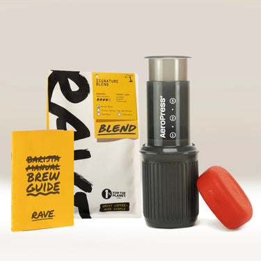 AeroPress Go Gift Set by Aeropress, featuring a black mug, red filter cap, yellow brew guide, and Rave coffee bag—arranged on a white background for the ultimate portable coffee brewing experience at home or on the go.