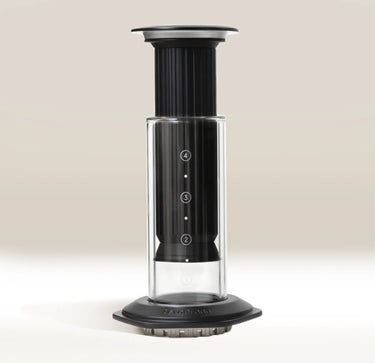 The Aerobie AeroPress Premium Coffee Maker, in black and clear plastic, stands upright on a neutral background. Its cylinder shows 2–4 measurement markings and features innovative 3-in-1 brew technology.