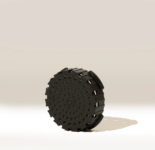 An Aeropress AeroPress Replacement Filter Cap, black and circular with side ridges and raised dots, stands upright on a light background with a shadow underneath.