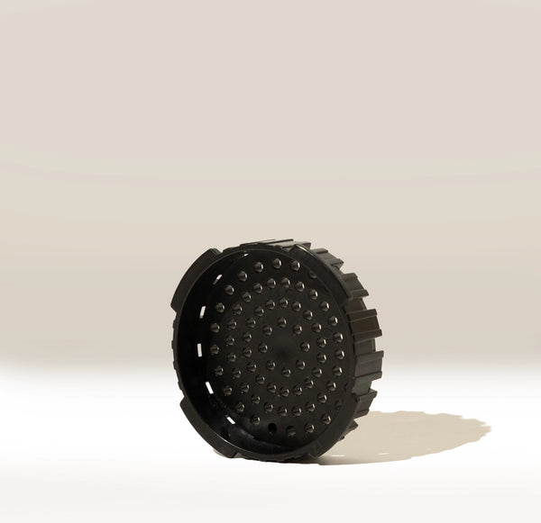 A black, round AeroPress Replacement Filter Cap by Aeropress, featuring textured sides and multiple holes, stands upright on a light background with a faint shadow.