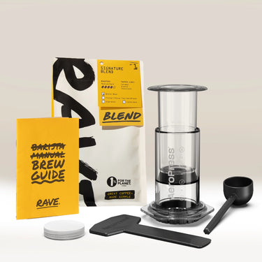 Introducing the Aeropress Gift Set Clear/Colour by Aeropress—featuring a premium coffee maker, a bag of fresh coffee beans, a vibrant yellow brew guide, coffee scoop, stirrer, paper filters, and filter holder. All components are neatly arranged on a light background, making this the ideal home coffee brewer and thoughtful gift for any coffee enthusiast.