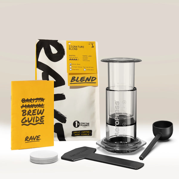 Introducing the Aeropress Gift Set Clear/Colour by Aeropress—featuring a premium coffee maker, a bag of fresh coffee beans, a vibrant yellow brew guide, coffee scoop, stirrer, paper filters, and filter holder. All components are neatly arranged on a light background, making this the ideal home coffee brewer and thoughtful gift for any coffee enthusiast.