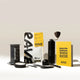 The AeroPress Gift Set with Grinder by Aeropress includes an AeroPress coffee maker, manual grinder, fresh roasted Rave coffee (yellow bag), black scoop, stirrer, filter holder, and a yellow brew guide—perfectly arranged on a light surface.