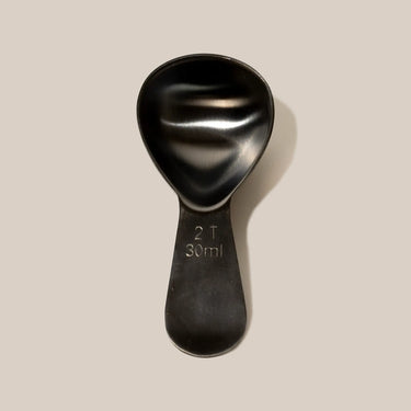 The Planetary Design Airscape Coffee Scoop is a black plastic scoop marked with 2 T and 30 ml, shown against a plain beige background—ideal for use with your Airscape tin or other stainless steel kitchenware.