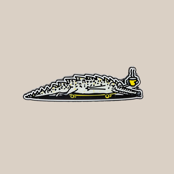 A relaxed crocodile illustration, inspired by the Rave Alligator Pin Badge from RAVE Coffee, features a yellow teacup balanced on its nose against a light beige background.