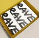 Three white rectangular boxes with large black brushstroke-style letters spelling 'RAVE' are arranged inside a mustard yellow shipping box on a light beige background.