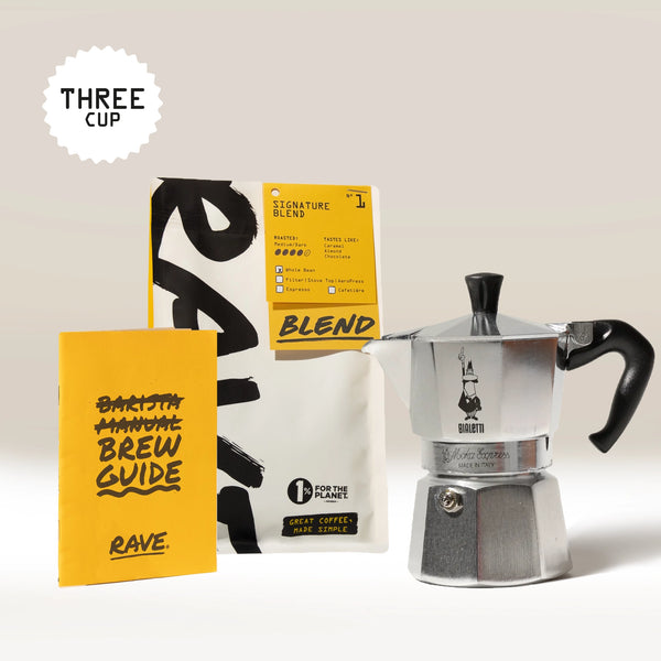 The Bialetti Moka Express Stove Top Gift Set by Bialetti is displayed against a light background, featuring the iconic Italian coffee maker alongside a coffee bag, a yellow brew guide, and a sign reading “THREE CUP.”.