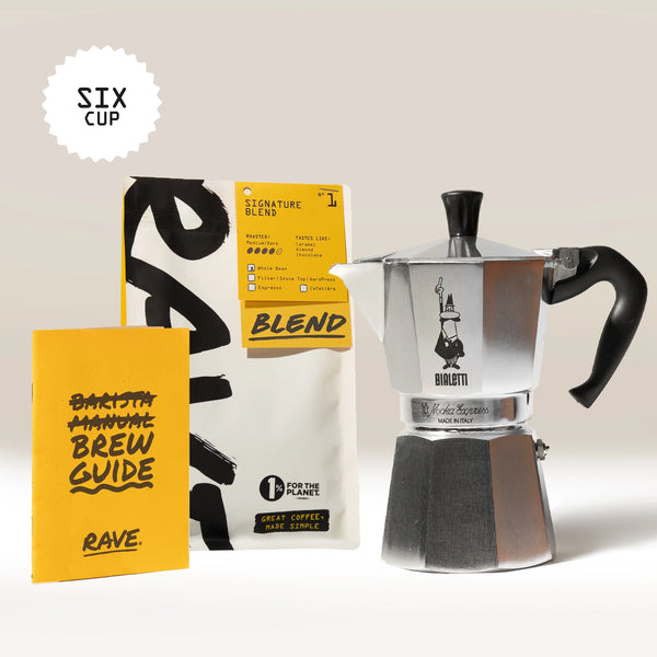 A Bialetti Moka Express Stove Top Gift Set by Bialetti, featuring a silver coffee maker, a bag of RAVE coffee beans labeled Blend, and a yellow brew guide, is displayed on a light surface. A "SIX CUP" label appears in the top left corner.