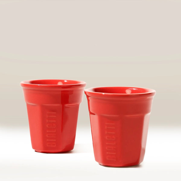 Two red ceramic espresso cups with "Bialetti" embossed vertically on the side rest on a plain light surface—ideal for enjoying coffee brewed with your Bialetti Mini Express Moka Pot.