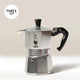 A Bialetti Moka Express Stove Top Coffee Maker in silver, featuring a black handle, is displayed against a plain background. A 