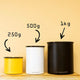 Three Planetary Design Airscape coffee storage containers—small yellow (250g), medium white (500g), and large black (1kg)—are displayed on wood, highlighting their airtight, oxygen-free technology. The large container is the Black Airscape.