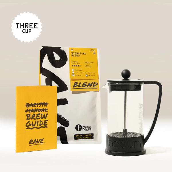 A Bodum French Press Gift Set by Bodum, featuring a yellow Brew Guide booklet and a bag of “Signature Blend” Rave Coffee beans, is displayed together on a light background—making the perfect coffee gift box. A Three Cup graphic is shown in the top left corner.