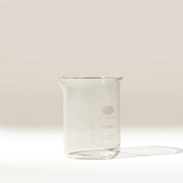 The Labtek Borosilicate Glass Beaker, 100ml with measurement markings, stands transparent on a white surface against a light beige background—perfect as an espresso shot catcher for accurate pours.