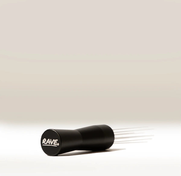 A black RAVE brand WDT tool with multiple thin metal prongs extending from one end, shown on a clean, light beige-to-white gradient background.