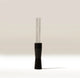 A modern coffee tool with a matte black handle and four slender stainless steel wires, standing upright on a clean white surface against a warm beige background.