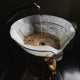 Hot water is being poured in a circular motion over ground coffee in a Chemex brewer with a white paper filter from the Chemex Gift Set by Chemex, brewing freshly roasted coffee.