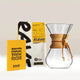 The Chemex Gift Set by Chemex, featuring a brewer, a yellow coffee guide booklet, a bag of Rave Signature Blend coffee, and a stack of Chemex filter papers, is displayed against a white background—an ideal starter pack for coffee enthusiasts and newcomers alike.
